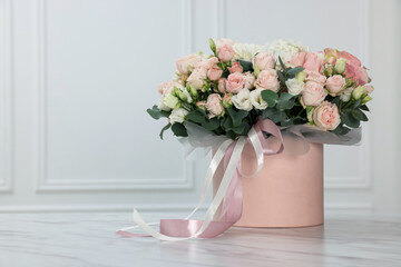Gift box with bouquet of beautiful flowers and eucalyptus branches on marble table against white wall. Space for text