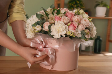 Florist with beautiful bouquet in box at table indoors, closeup