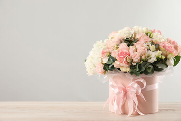 Beautiful bouquet in box on wooden table against light background. Space for text
