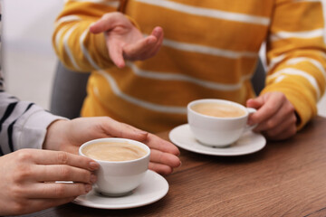 Coffee break. Women with cups of hot drinks at wooden table indoors, closeup