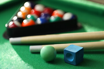 Many colorful billiard balls in triangle rack, cues and chalk on green table, closeup