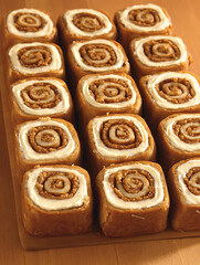 Fototapeta premium Rows of freshly baked cinnamon rolls glazed with creamy frosting arranged neatly on a wooden board perfect for sharing.