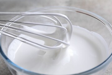 Whisking whipped cream in bowl on grey table, closeup