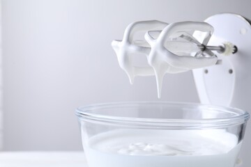 Hand mixer with whisks and bowl of whipped cream on white table, closeup. Space for text