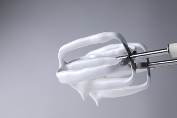 Hand mixer with whisks and whipped cream on grey background, closeup