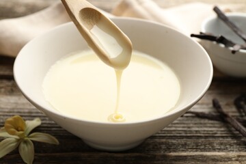 Taking tasty vanilla condensed milk with spoon from bowl on wooden table, closeup
