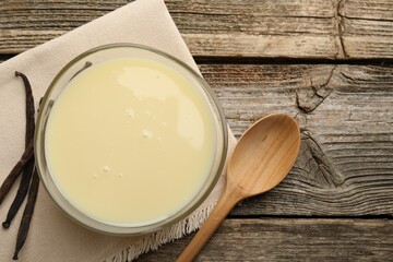 Tasty condensed milk, spoon and vanilla pods on wooden table, flat lay