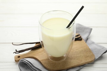 Delicious vanilla milk in glass and pods on white wooden table, closeup