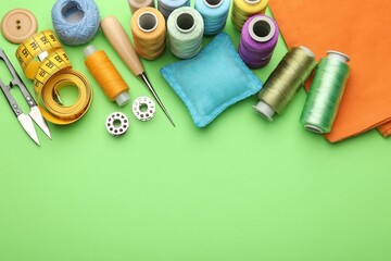Different sewing supplies on green background, flat lay. Space for text