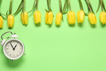 Spring time. Alarm clock and beautiful tulips on green background, flat lay. Space for text