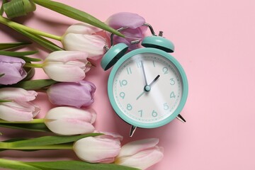 Spring time. Alarm clock and beautiful tulips on pink background, flat lay