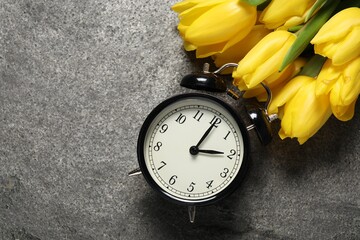 Spring time. Alarm clock and beautiful tulips on grey table, flat lay. Space for text