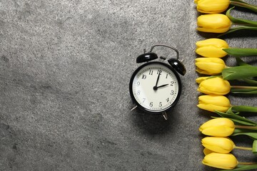Spring time. Alarm clock and beautiful tulips on grey table, flat lay. Space for text
