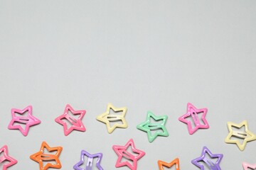 Colorful star shaped hair clips on light grey background, flat lay. Space for text