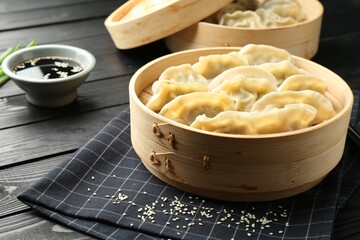 Tasty boiled gyoza (dumplings) with soy sauce and sesame on black wooden table