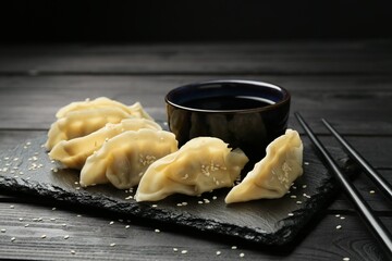 Tasty boiled gyoza (dumplings) served on black wooden table, closeup