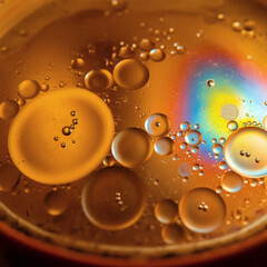 Close up of golden oil droplets in water with colorful reflections, abstract macro photography
