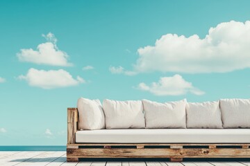 青空の下でリラックスできる木製ソファが海に面したテラスに設置されている情景