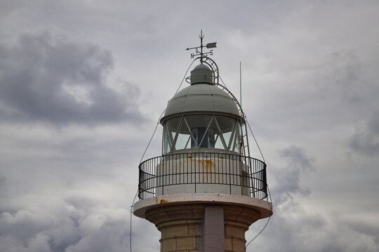 Detail of the top of the Torco lighthouse with its weather vane and lightning rod in the town of Suances in Cantabria, on a cloudy day at sunset. Concept travel, coast, cliffs, destinations, sea.