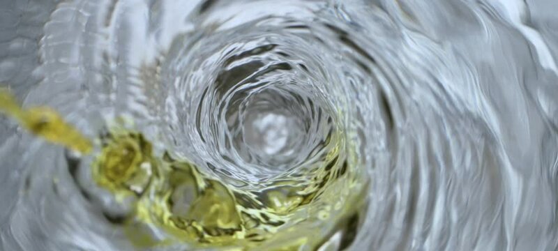 Top down view of golden colored chemical falling in water vortex, creating tunnel shape in slow-motion