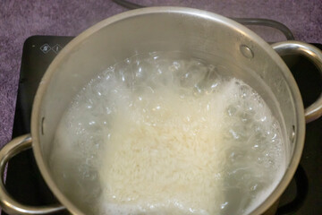 A pot filled with boiling water and rice cooking. The steam rises, creating a warm and inviting atmosphere, perfect for promoting cooking and culinary experiences.