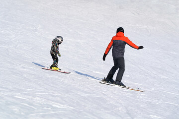 Teaching a child to ski on alpine skis. A man shows a little boy how to keep his balance.