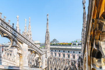 The ornate rooftop of Milan's Duomo features intricate spires and statues under a clear blue sky,...