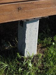 A cement post is in the grass next to a wooden bench. The bench is empty