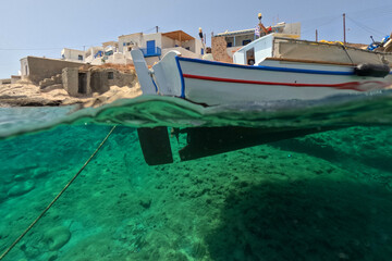 Underwater split photo of traditional fishing boat anchored in small cove of Goupa Kara famous for colourful boat houses called Sirmata, Kimolos island, Cyclades, Greece