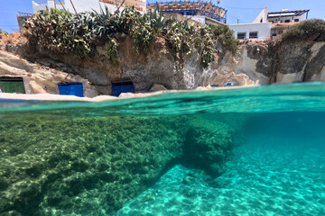 Underwater split photo of small cove of Goupa Kara famous for colourful boat houses called Sirmata, Kimolos island, Cyclades, Greece