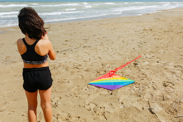 rea view of dark haired girl with rainbow kite on the beach