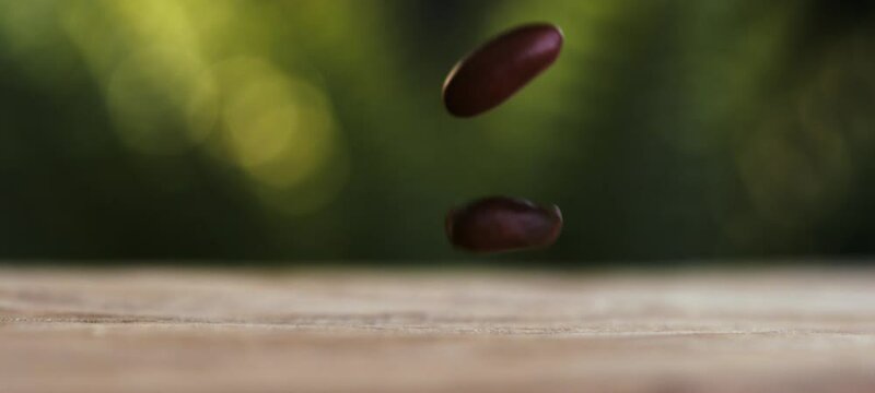 A dynamic display of red miki beans falling down on the wooden table against a green blurry background. Slow-motion footage