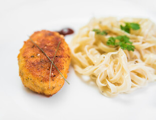 Meat cutlet with noodles and greens on a white plate
