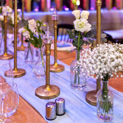 Wedding table setting with plates, blue napkins, wine glasses, and bouquets of lisianthus and gypsophila, along with kerosene lamps for a wedding event.
