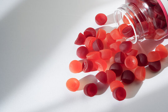 A transparent bottle spills red and orange gummy vitamins onto a clean, white surface