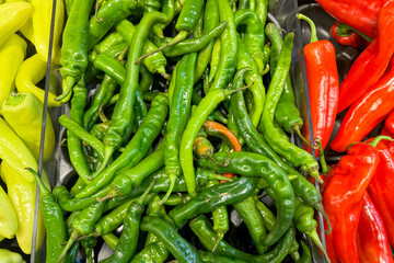 A vibrant display of fresh green, red, and yellow chili peppers arranged in a grocery store