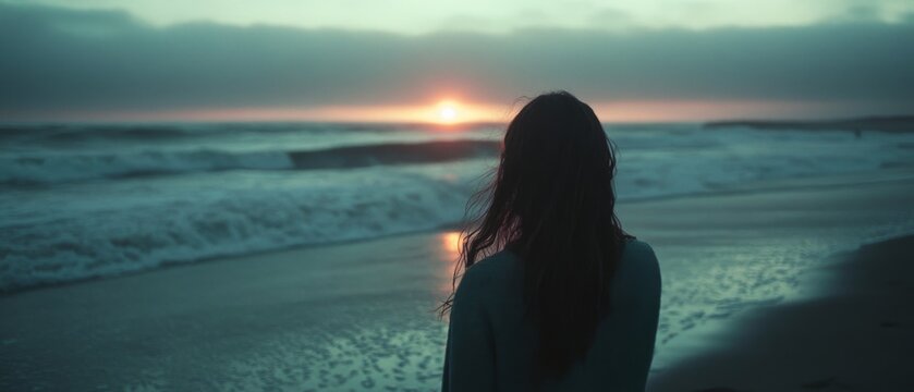 Silhouette of a woman standing on a beach, gazing at a serene sunset, encapsulating hope and contemplation.