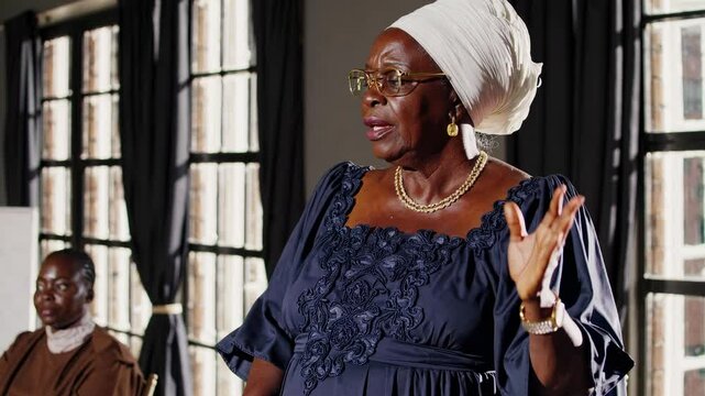 A mid-shot video captures an elderly woman in elegant attire, standing by large windows, with soft natural light highlighting her dignified presence.