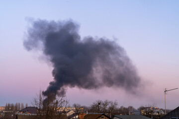 hick black smoke rising into the sky over residential buildings and trees at dusk. Environmental...