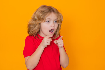 Fototapeta premium Excited kid boy pointing away finger on yellow background. Child pointing to copyspace, showing promo offers, points away. Surprised face, amazed emotions of child.