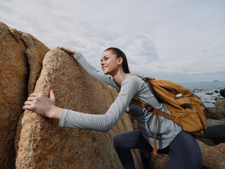 Young female hiker in sportswear climbing rocks, showcasing determination and adventure, with a...
