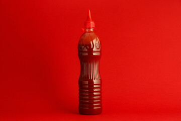 Ketchup in plastic bottle on red background