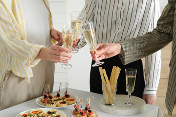 Many different tasty canapes on white table. People clinking glasses of wine indoors, closeup