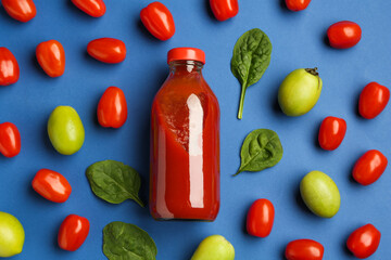Tasty ketchup in bottle, tomatoes and basil on blue background, flat lay