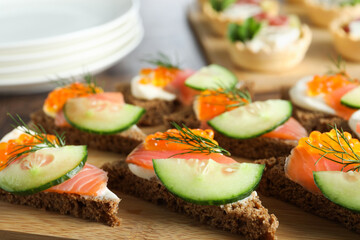 Tasty canapes with salmon and cucumber on wooden table, closeup