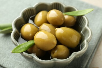 Delicious marinated olives in bowl and green leaves on table, closeup