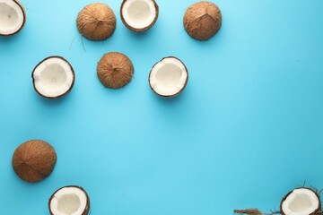 Halves of fresh coconuts on light blue background, flat lay. Space for text