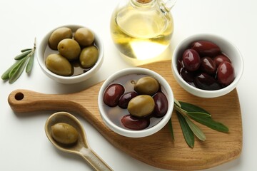 Tasty marinated olives, leaves and oil on white table, closeup