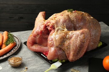 Whole raw turkey with ingredients for marinade and other products on grey table