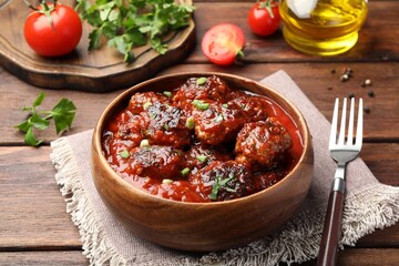 Delicious meatballs with tomato sauce and herbs served on wooden table, closeup